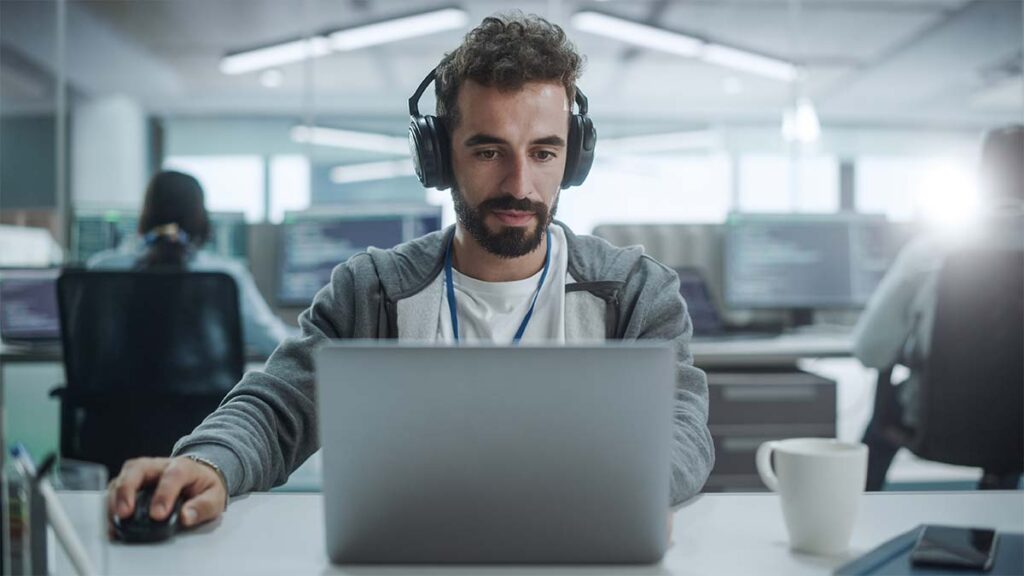 A man wearing headphones while working on a laptop in an office