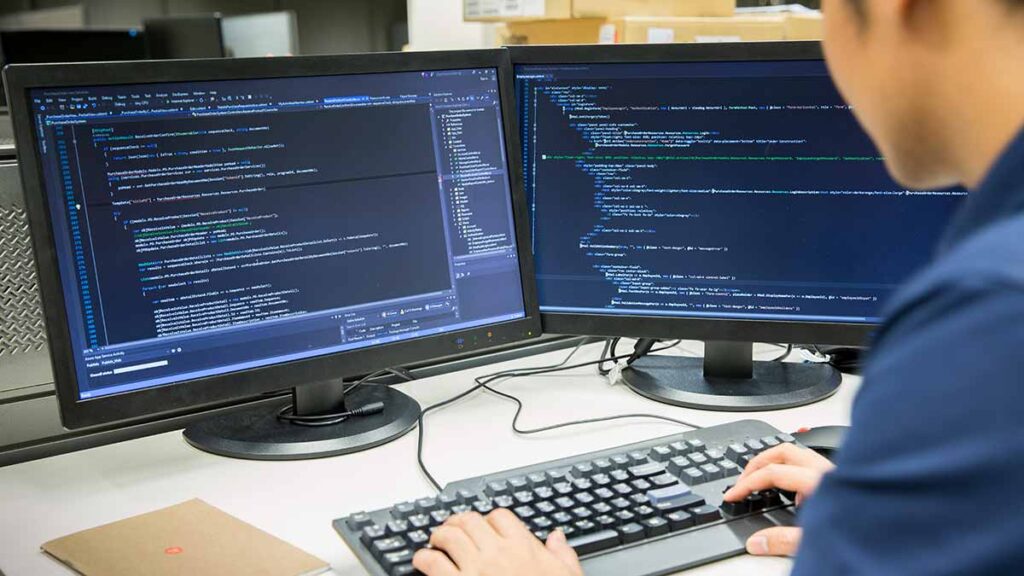 A male programmer looking at computer monitors with lines of code