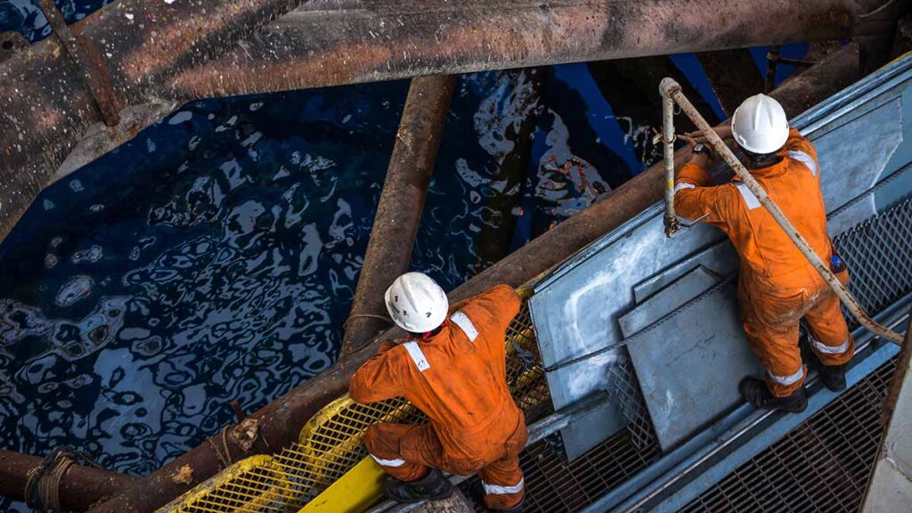 Offshore oil rig workers looking down from a platform into the sea