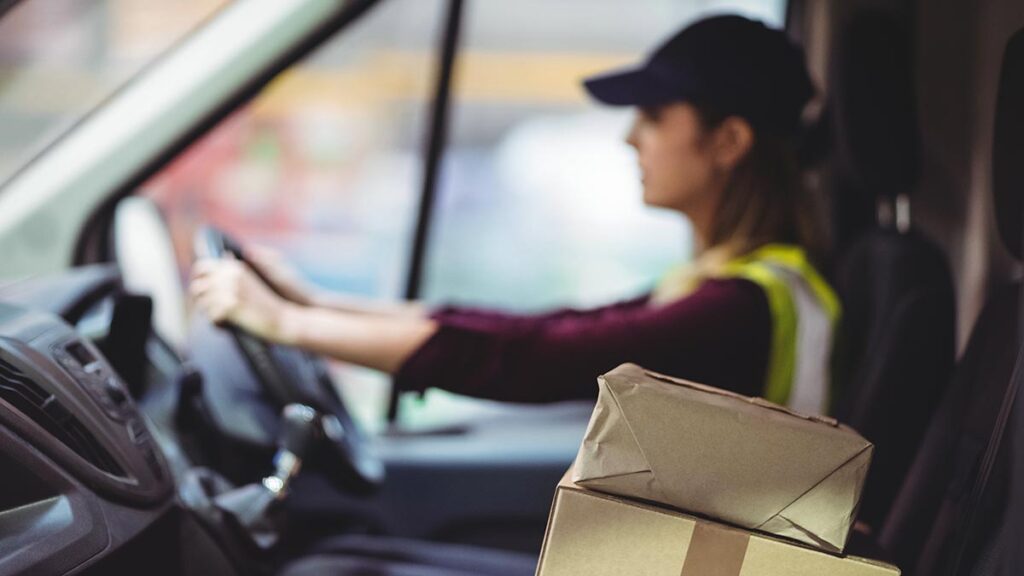 A woman driving a delivery van with boxes on the seat beside her