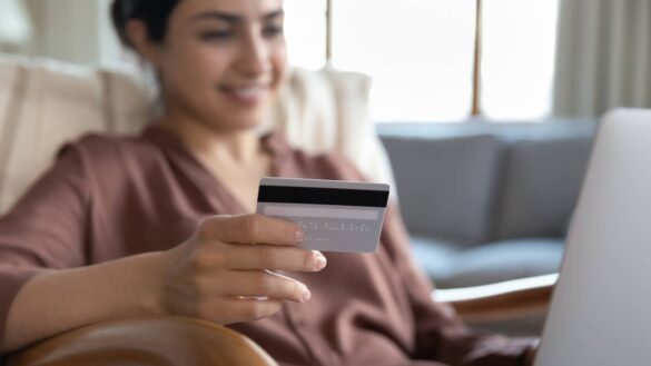 A woman holding a credit card while using a laptop