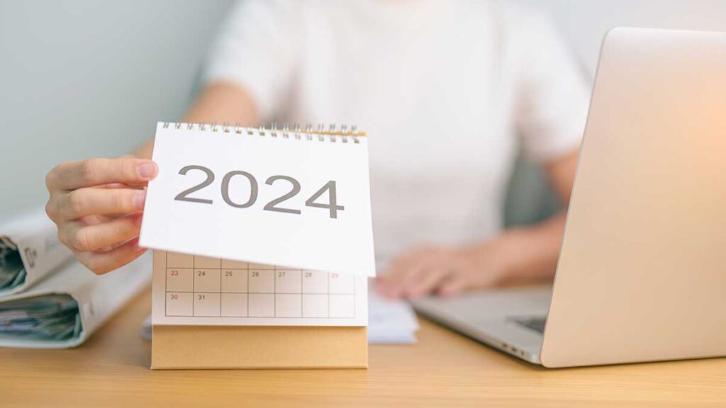 A person turning over a sheet on a desk calendar with '2024' on the paper