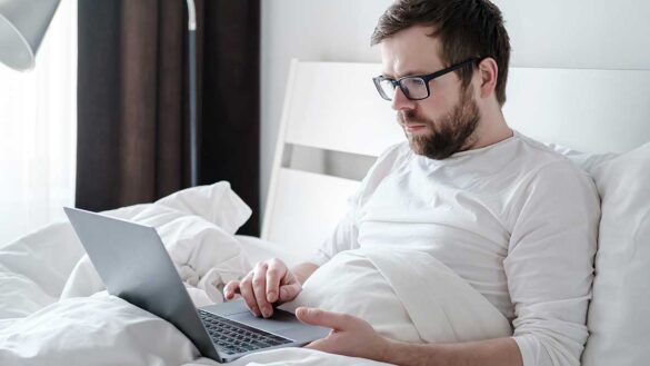 A man working on a laptop whilst in bed