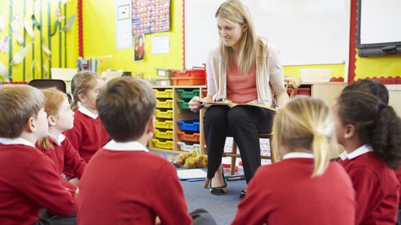 A primary school teacher reading to children sitting in a circle