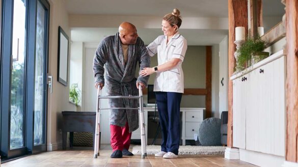 A care worker helping an elderly man with a walking frame