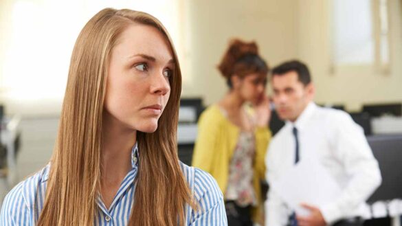 A woman looking back at colleagues gossiping about her, in the background. Neurodiversity discrimination