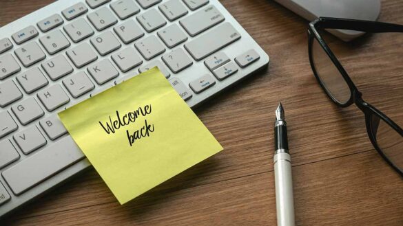 Return to work: 'Welcome back' written on a sticky note, which has been stuck to a keyboard on a desk