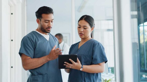 Two nurses looking at a tablet in a hospital corridor