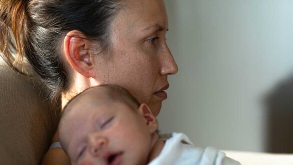 Worried mother with a sleeping baby on her shoulder