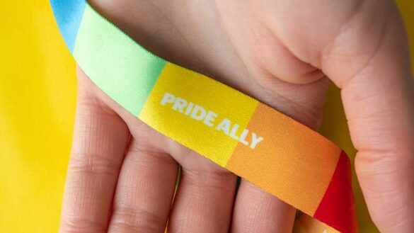 A rainbow lanyard in a person's hand, with 'pride ally' written on it