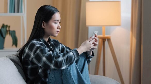 A young woman sitting on a sofa and looking at her phone