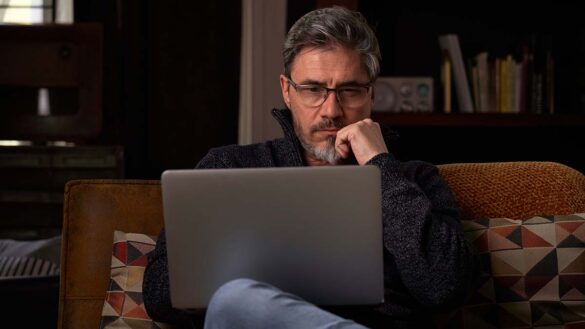 A man looking bored at home while using a laptop
