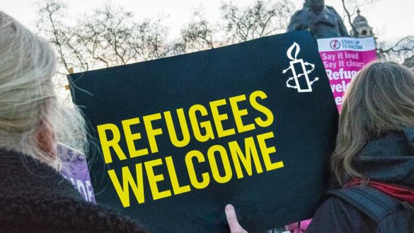 A woman holding a sign saying 'refugees welcome' during a protest