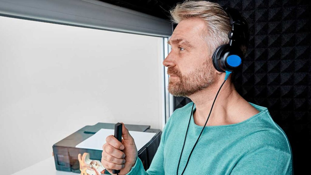 A man wearing headphones in a booth, while undertaking an audiogram assessment for hearing loss