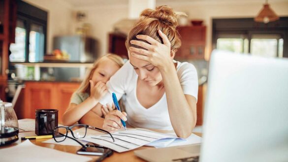 A woman looking over paperwork with her head in her hands, while a young girl is comforting her.