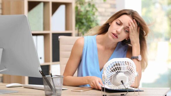 woman switches on a fan in a hot office