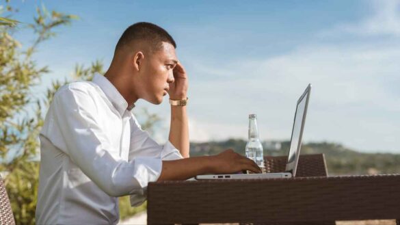 Young man working on laptop in a pub beer garden or his own garden with a bottle of beer beside him