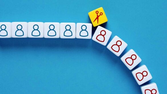 reduce headcount NICs job cuts. Photo shows an illustration of job cuts dice representing people and a pair of scissors.