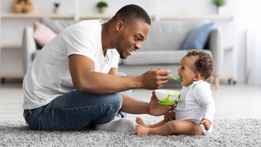 Equal parental leave. Photo shows a dad spoon-feeding his baby.