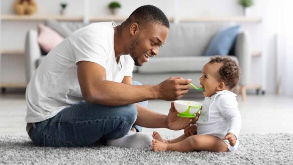 Equal parental leave. Photo shows a dad spoon-feeding his baby.