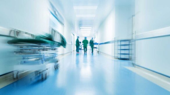 NHS agency worker ban staff retention: Photo shows a blurred hospital corridor with clinical staff.